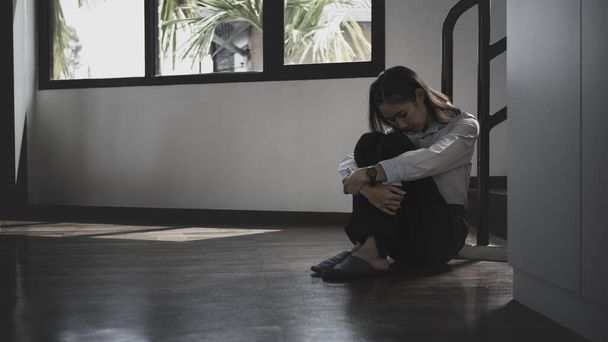 Mujer joven y solitaria sentada en el suelo en una habitación oscura con sensación de tristeza y depresión. - Foto, Imagen