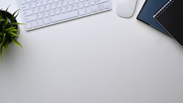 ワイヤレスキーボード、ハウスプラント、ノートブック広告コピースペース付きホワイトオフィスデスクのトップビュー. - 写真・画像