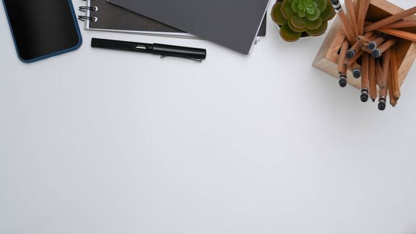 白い机の上にスマートフォン、ノートブック、文房具、植物やコピースペースでデザイナーの職場のオーバーヘッドショット. - 写真・画像