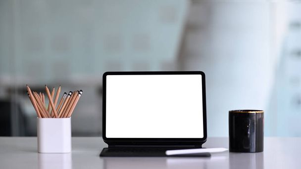 Vista frontal de la tableta del ordenador con pantalla vacía, portalápices y taza de café en el escritorio de la oficina blanca. - Foto, imagen