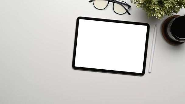 Κάτοψη του digital tablet με άδεια οθόνη, γυαλιά, φλυτζάνι καφέ και φυτό σε λευκό γραφείο. - Φωτογραφία, εικόνα