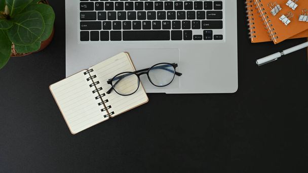 Musta toimisto työpöytä kannettava tietokone, muistikirja, silmälasit ja kynä house kasvi. - Valokuva, kuva