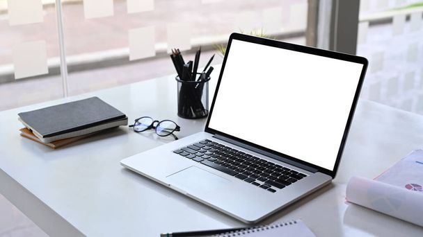 Moderner Arbeitsplatz mit Computer-Laptop, Bleistifthalter, Dokument, Brille und Notizbuch auf weißem Schreibtisch. - Foto, Bild