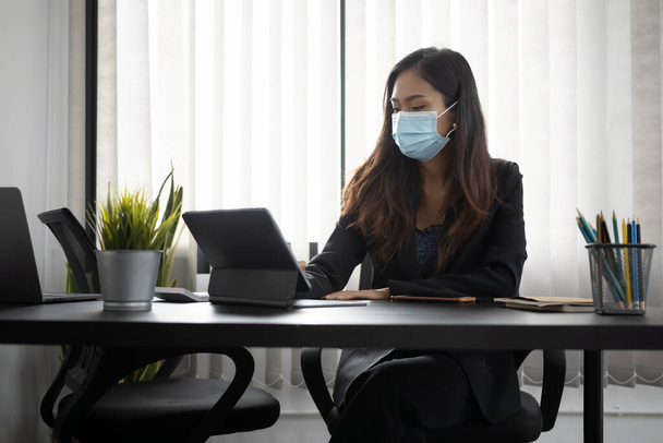 Mujer de negocios en la máscara protectora concentrado de trabajo en la tableta de ordenador en el escritorio de la oficina. - Foto, Imagen