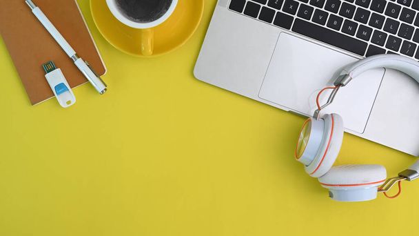 Рабочее пространство с ноутбуком, чашкой кофе, наушниками и ноутбуком на желтом фоне. - Фото, изображение