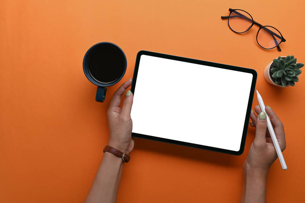 Вид сверху женщины, держащей цифровой планшет и перо стилуса на оранжевом фоне. - Фото, изображение