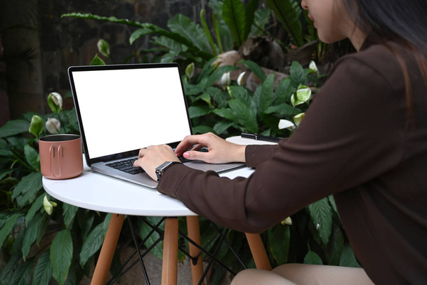 Colpo ritagliato femminile digitando computer portatile a schermo vuoto sul tavolo nel parco. - Foto, immagini