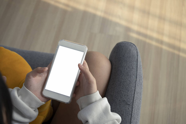 Zblízka pohled na mladou ženu držící maketu až chytrý telefon s prázdnou obrazovkou, zatímco sedí na gauči doma. - Fotografie, Obrázek