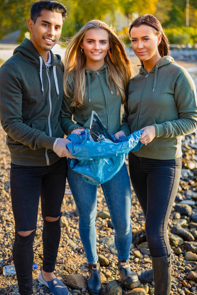 Equipe sorridente de voluntários segurando saco de lixo na praia - Foto, Imagem