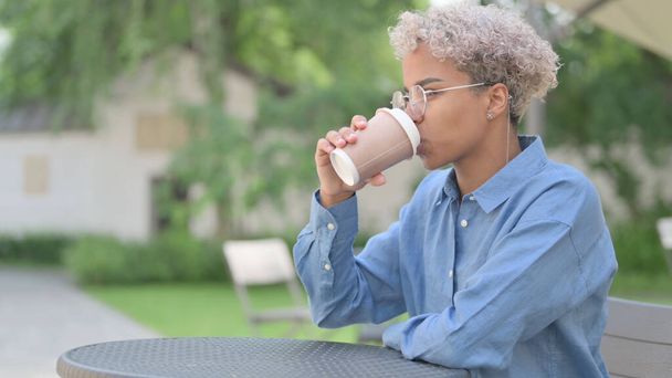 アフリカ人女性が屋外カフェでコーヒーを飲む  - 写真・画像