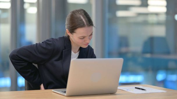 Genç iş kadını dizüstü bilgisayar kullanırken sırt ağrısı çekiyor - Fotoğraf, Görsel