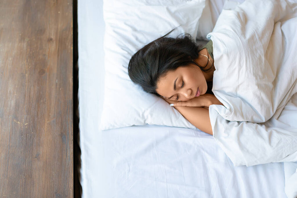 Vista dall'alto di una donna asiatica addormentata. Si sdraia sotto il piumone e abbraccia il cuscino. - Foto, immagini