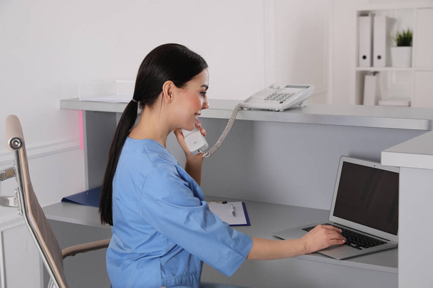 Receptionist talking on phone at workplace in hospital - Photo, Image