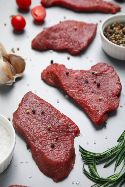 Fresh raw meat steaks and spices on light grey table - 写真・画像