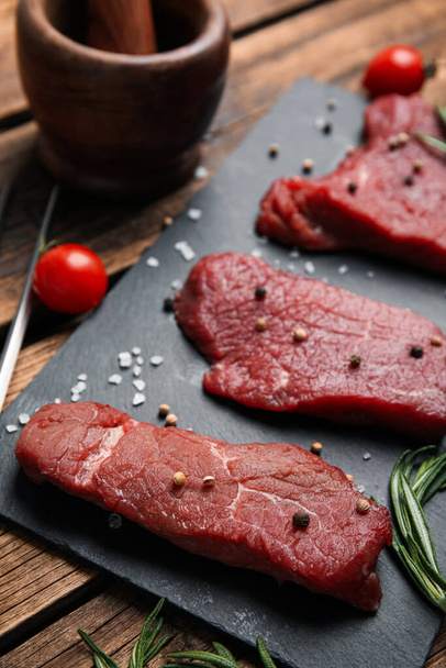 Fresh raw meat steaks and spices on wooden table, closeup - Фото, изображение
