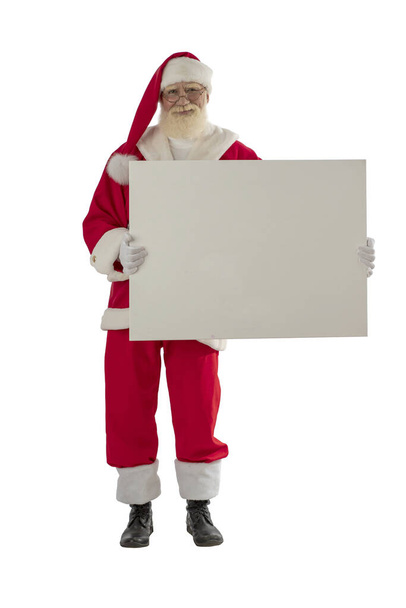 Santa Claus on white background isolated. Senior actor old man with a real white beard in the role of Father Christmas holding a mock up board. Male character stands upright full-length - Photo, Image