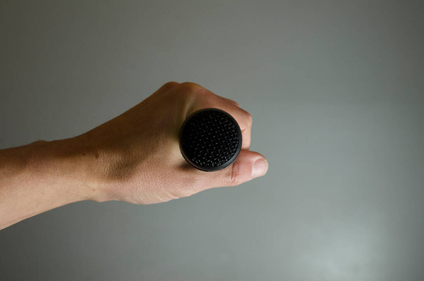 black microphone in hand, from front isolated on gray background wanting to communicate, concept of expression, journalism, freedom of communication - Foto, afbeelding