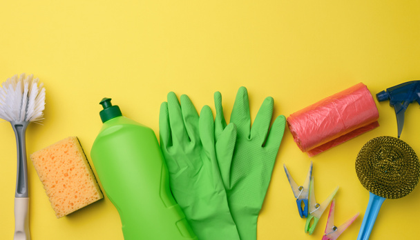 зеленые резиновые перчатки для чистки, красная мусорная корзина пластиковый рулон и пластиковая бутылка с моющим средством, щетка на желтом фоне, набор, вид сверху - Фото, изображение