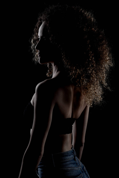 Side lit brunette girl with long curly hair, silhouette studio portrait on dark background. - Photo, image