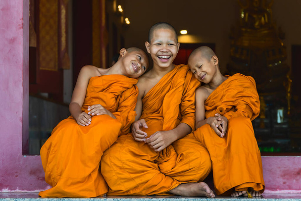 three Thai buddhist novice monk smiling and sitting together at temple gate  - Foto, Imagen
