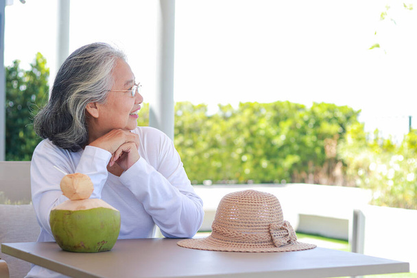 白いシャツを着た幸せなアジアの高齢者の女性座って、涼しい自然の風をお楽しみください。高齢者のための観光の概念は、リラックスして退職して幸せになるために住んでいます。コピースペース - 写真・画像