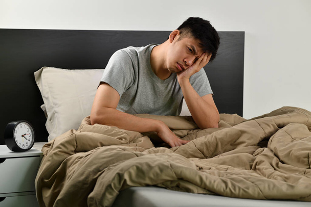 Depressieve jonge Aziatische man zit in bed kan niet slapen van slapeloosheid - Foto, afbeelding