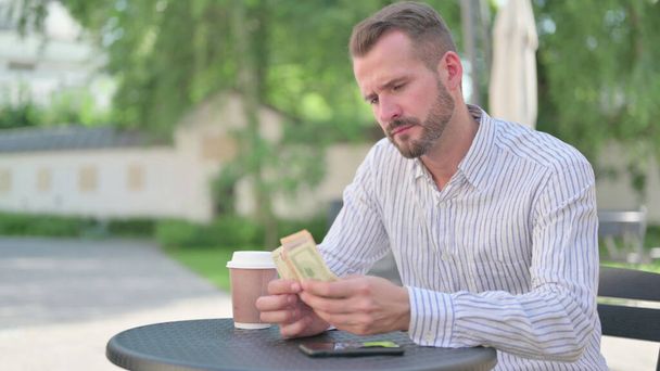 Hombre adulto maduro contando dólares mientras está sentado en el café al aire libre - Foto, Imagen