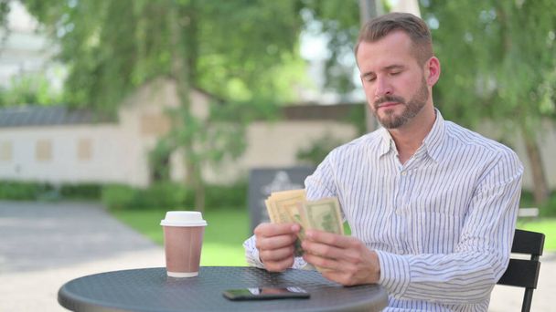 Mature Adult Man Feeling Happy while Counting Dollars in Outdoor Cafe - Foto, imagen