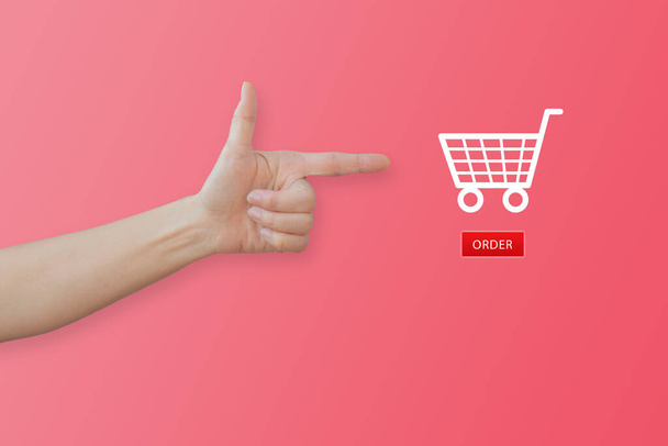 Ostokset Online Concept: Käsi eleiden ja osoittaa ostoskorin kuvaketta vaaleanpunainen tausta. - Valokuva, kuva