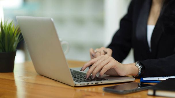 Zamknij biznes kobieta w czarnym garniturze, ręce wpisując na klawiaturze laptopa w miejscu pracy przeglądając informacje biznesowe - Zdjęcie, obraz