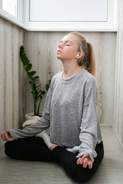 Jonge millennial blonde vrouw doen yoga oefening luisteren audio tutorial met koptelefoon stretching fitness op balkon huis. Mindfulness meditatie. Het concept van online training. Videoles - Foto, afbeelding