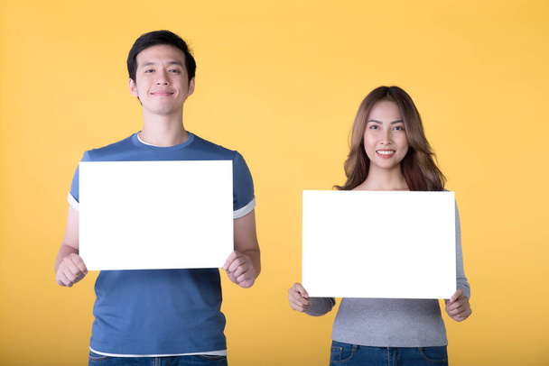Asian couple holding empty blank boards and smiling at camera isolated on yellow background - Photo, image