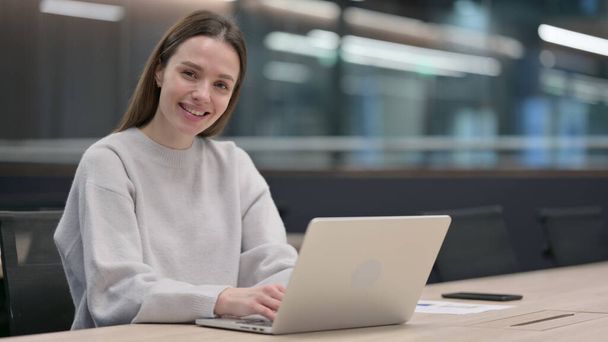 Frau lächelt während der Arbeit am Laptop in die Kamera - Foto, Bild