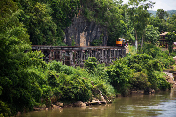 Tren que corre por la pista entre la montaña del paso del fuego del infierno y la cascada de Sai Yok junto al río Khwae traen a la gente tailandesa y los viajeros extranjeros visitan la cueva de Tham krasae en Kanchanaburi, Tailandia - Foto, imagen