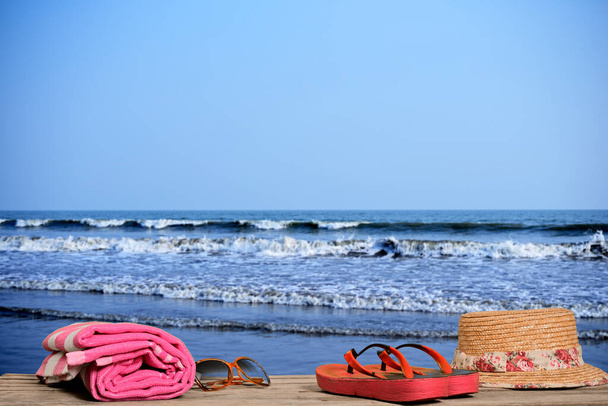 Žabky, osušky, sluneční brýle a klobouk na dřevěné lavičce na pláži. - Fotografie, Obrázek