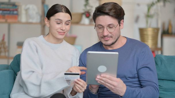 Casal de raça mista fazendo compras on-line bem sucedidas em Tablet em casa - Foto, Imagem
