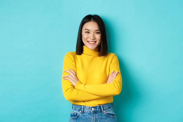 Confident and stylish asian woman cross arms on chest and smiling, standing over blue background - Foto, immagini