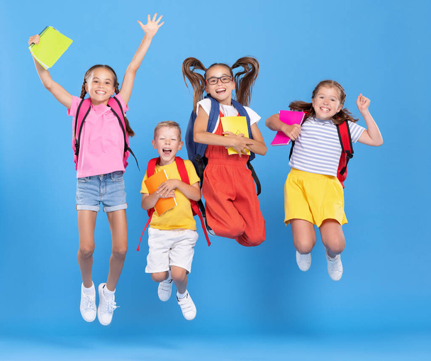 Gruppe lustiger aufgeregter Klassenkameraden in lässiger Kleidung mit Rucksäcken und Heften, die Spaß haben und auf blauem Hintergrund springen - Foto, Bild