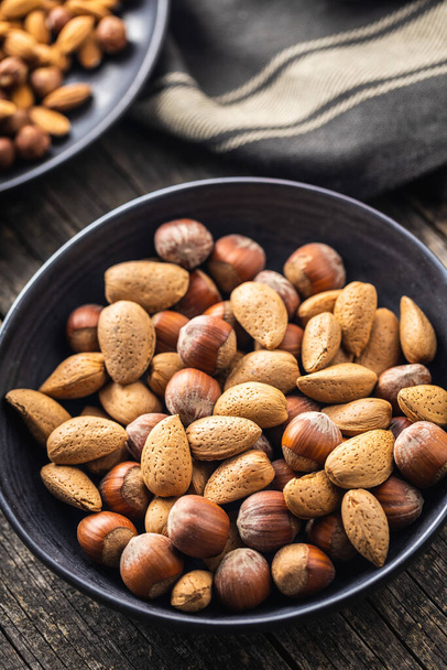 Unpeeled hazelnuts and almonds. Sweet nuts in bowl on black table. - Fotografie, Obrázek