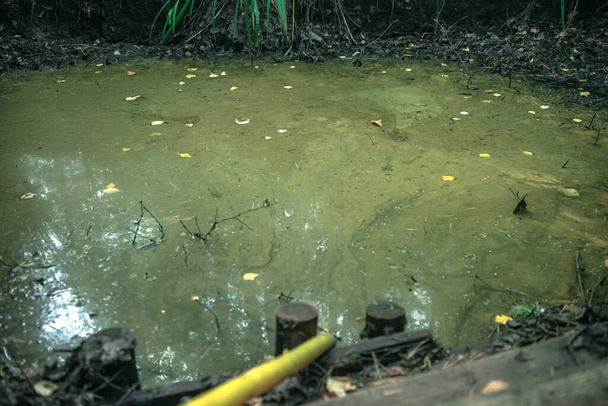 Ein großes, schmutziges, tiefes Loch im Boden, aus dem ein gelber Schlauch zum Abpumpen von Wasser ragt - Foto, Bild