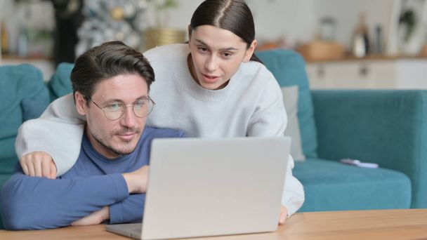 Amar a la pareja de razas mixtas sentados juntos y usando el ordenador portátil en casa  - Foto, imagen