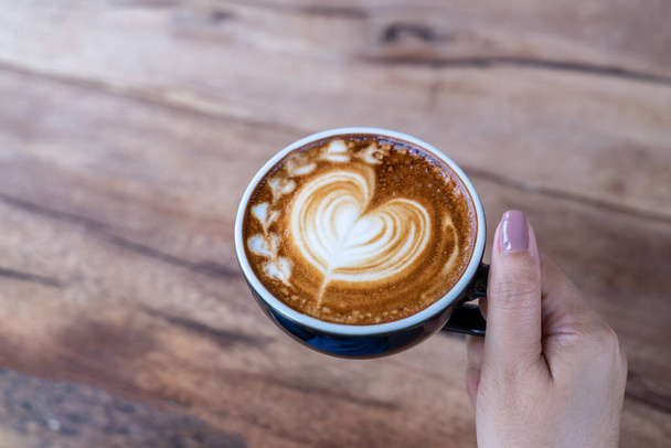 Nahaufnahme einer Tasse Kaffee-Latte-Art an der Hand einer Frau im Café eines Cafés - Foto, Bild