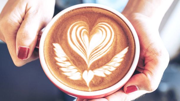 Close-up de uma xícara vermelha de café arte latte na mão da mulher no café da cafeteria - Foto, Imagem