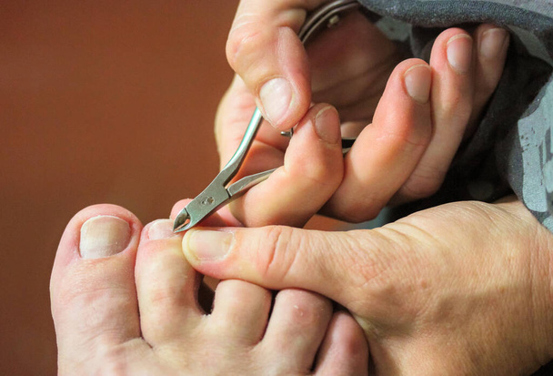 Manicure master w procesie pracy przycinanie naskórków na palcach nożyczkami pedicure, nożyce do wrastających paznokci. Zbliżenie ręce i nogi widok. Dzień Spa. Pielęgnacja paznokci w salonie. - Zdjęcie, obraz