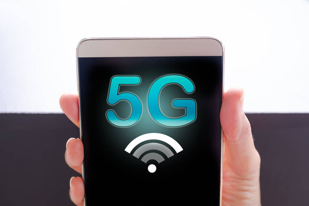 5Gシンボルを持つ携帯電話を手に持ち、黒と白の背景で閉じます。空白の空きスペースタッチスクリーンスマートフォン。技術信号無線高速インターネットwifi 5G,将来のビジネスコンセプト. - 写真・画像