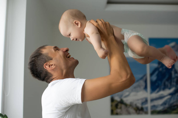 Father Hugging Newborn Baby in white bedroom. - Valokuva, kuva
