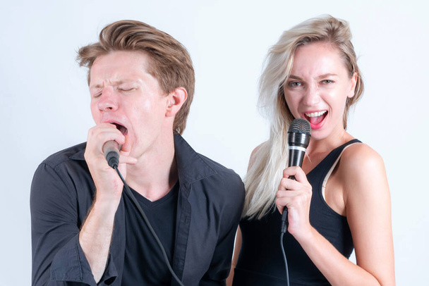 Χαρούμενο ζευγάρι χρησιμοποιώντας μικρόφωνο για να τραγουδήσει ένα τραγούδι καραόκε μαζί σε λευκό φόντο - Φωτογραφία, εικόνα