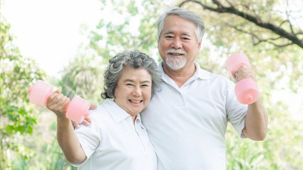 Счастливая любовь пожилого азиатского мужчины и пожилой азиатской женщины с гантелями для тренировок в парке, Они улыбаются с хорошим здоровьем вместе - Пожилая пожилая пара концепция - Фото, изображение