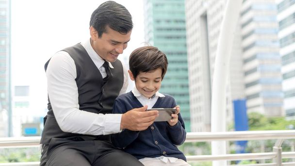 Père et fils jouant au téléphone intelligent ensemble sur le quartier des affaires urbain, concept de famille heureux papa et fils - Photo, image