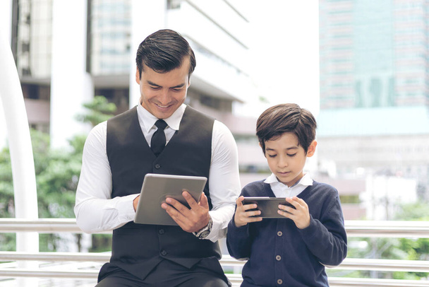 Padre e hijo jugando el teléfono inteligente del juego juntos en el distrito de negocios urbano, papá e hijo feliz concepto de familia - Foto, imagen